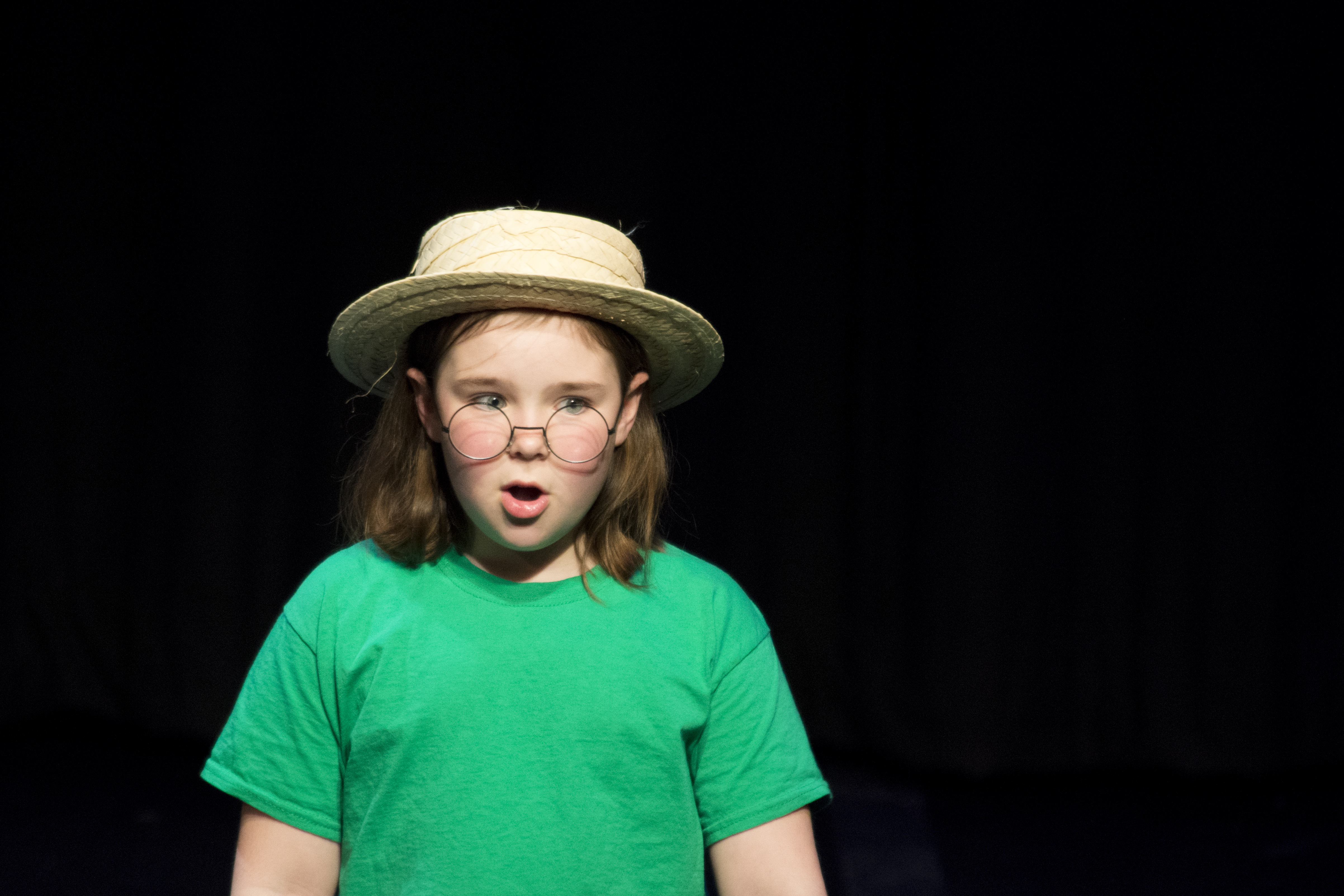 A young girl in a straw hat and blue dress performing on stage.