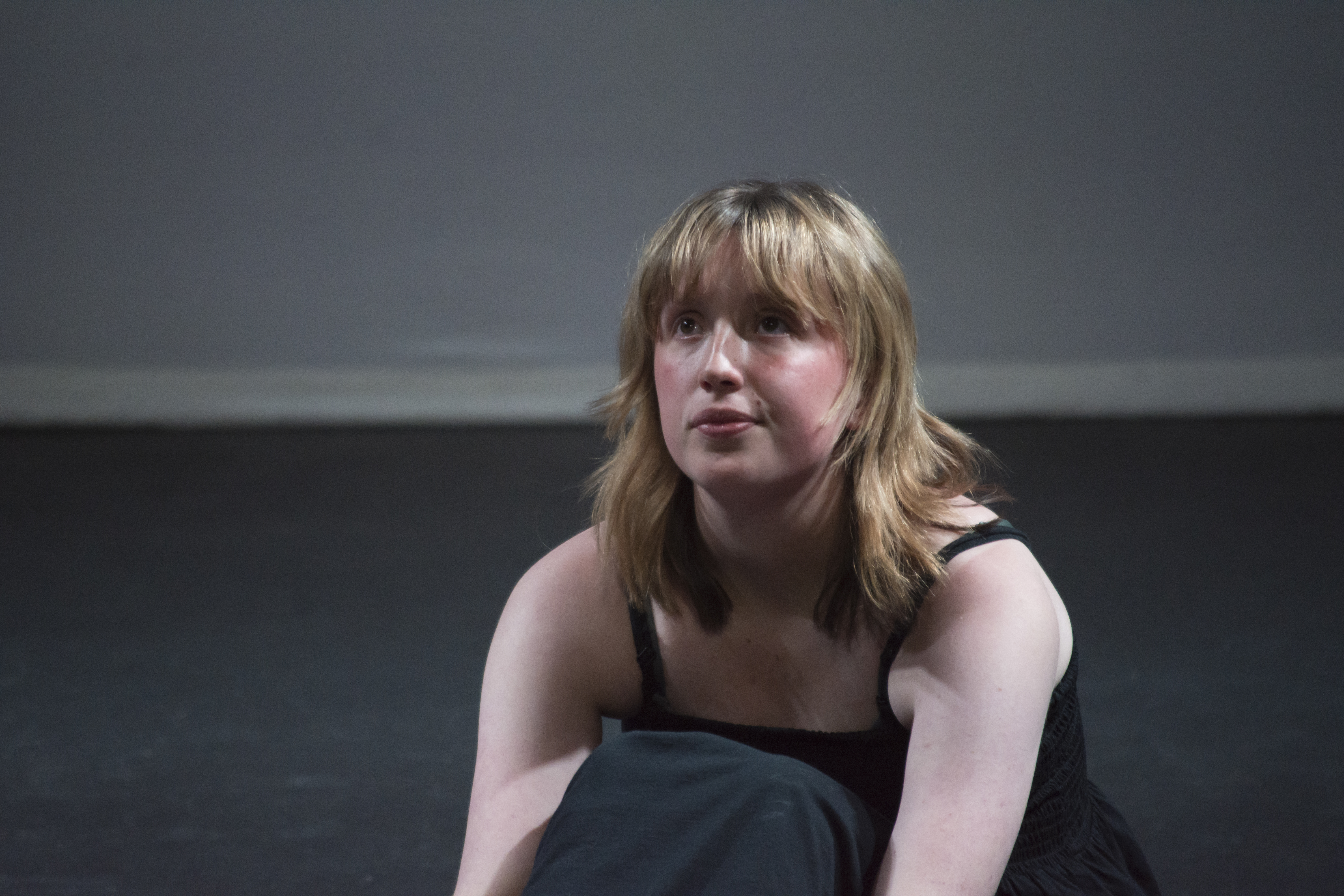 Young woman in a black outfit sitting on a stage, looking focused.